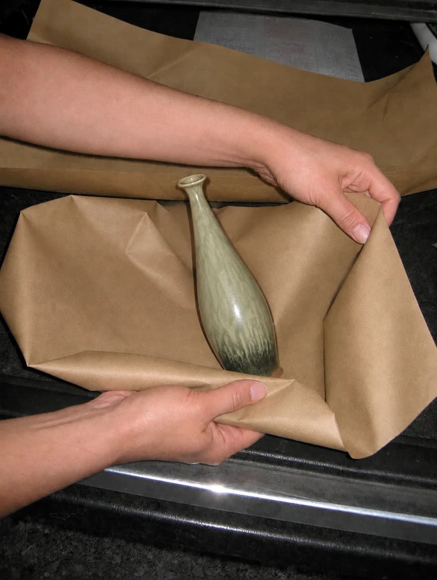 Hands wrapping a sage vase in kraft paper on a car tailgate